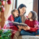 Mother reading to daughters by christmas tress