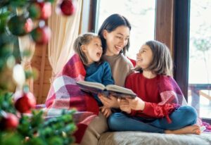 Mother reading to daughters by christmas tress