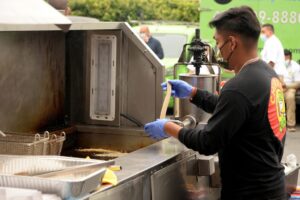 A man in a black shirt and blue gloves prepares food at an event in San Jose, CA.
