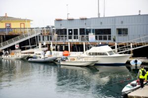 A man stands on a dock in San Jose, CA, beside a boat, enjoying waterfront view.