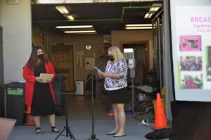 Two masked women stand in front of a screen in San Jose, CA, engaged in conversation.