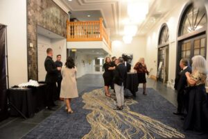 A group of people gather in a hallway featuring a large rug, set in San Jose, CA.