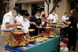 A group of masked and gloved individuals serving tacos at a food event in San Jose, CA.